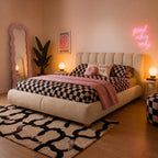 Beige ottoman bed with rounded tufted headboard, checkered duvet and pillows.